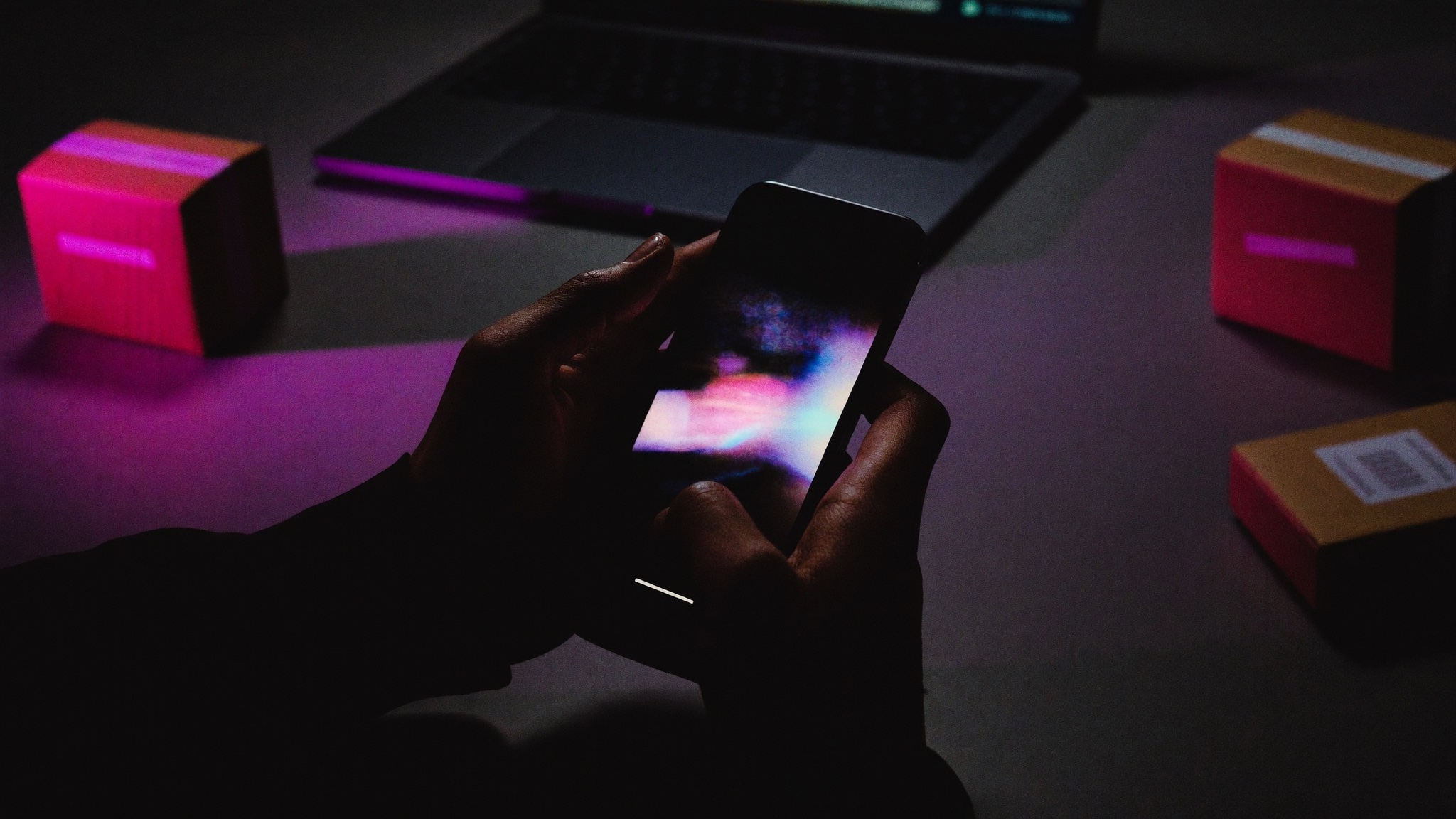 Mani con smartphone sopra una scrivania con pacchi e laptop: il recesso online con un clic
